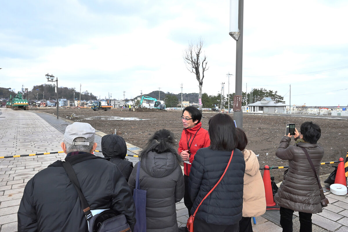 更地になった輪島市河井町本町の朝市通りで、バスツアーの団体客を案内する富水さん（2025年1月撮影）